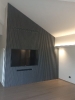 Boiserie in legno grigio con televisore a schermo piatto spento inserito al suo interno e porta inserita in un soggiorno mansardato_1