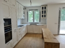 Cucina in legno di colore bianco con isola centrale in legno, inquadratura dal corridoio con vista sul piano lavabo e finestra_1