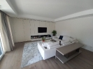 Panoramica soggiorno con mobili di colore bianco divano angolare in tessuto di colore bianco e televisore a schermo piatto appeso al mobile_1